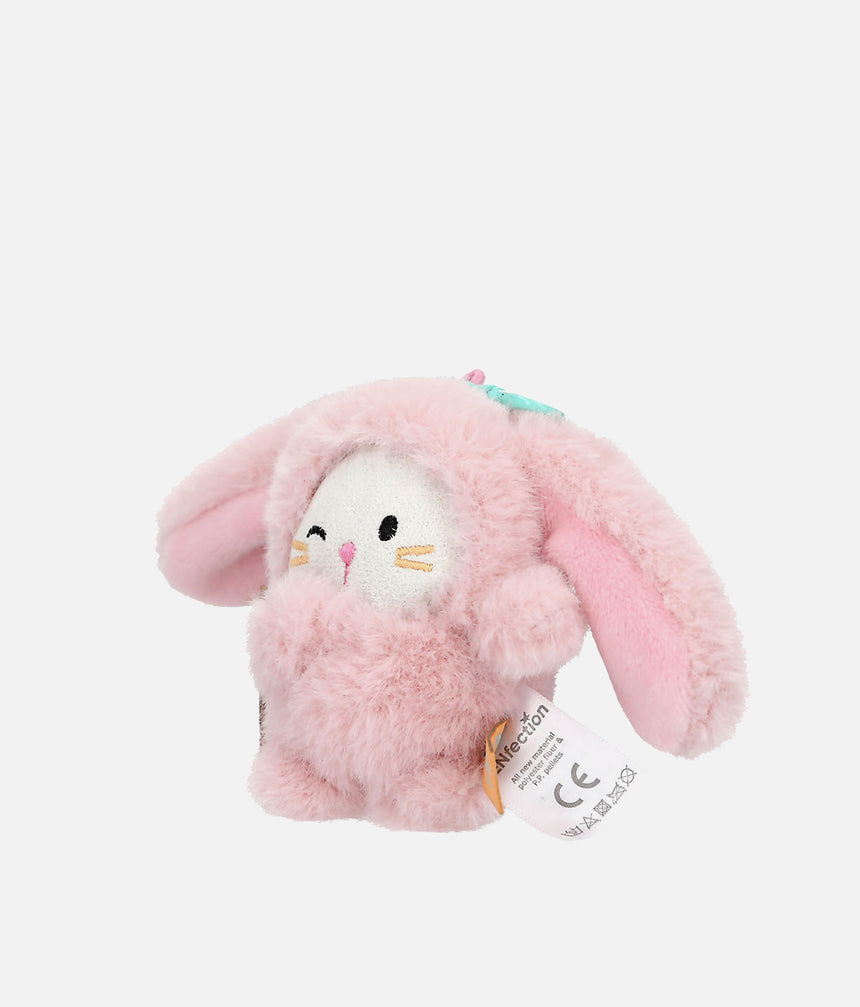 A small plush bunny toy in light pink with a white face, black embroidered eyes and nose, and a small turquoise bow on top. A white product tag is attached on the right side.