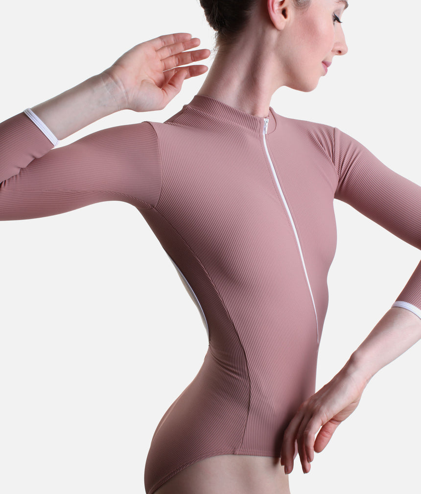 A model wearing a dusty rose pink long-sleeve dance leotard with a white center zipper and white trim on the cuffs, shown from a side profile against a light gray background.