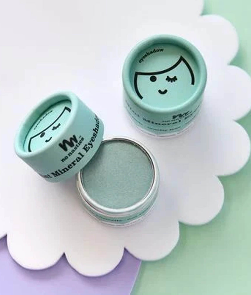 Three small round cosmetic jars of mineral eyeshadow arranged on a white scalloped tray. One jar is open, showing a pale mint green eyeshadow pan, while the other two are closed with light aqua lids featuring a simple black face illustration and the text 'mineral eyeshadow' and 'eyeshadow'.