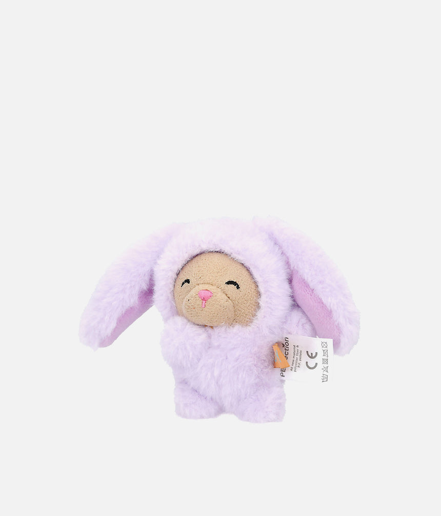 A small plush bunny toy in a fuzzy light purple or lavender bunny suit, with a beige stitched face, pink nose and mouth, and a small sewn tag attached on the right side, photographed on a plain light gray background.
