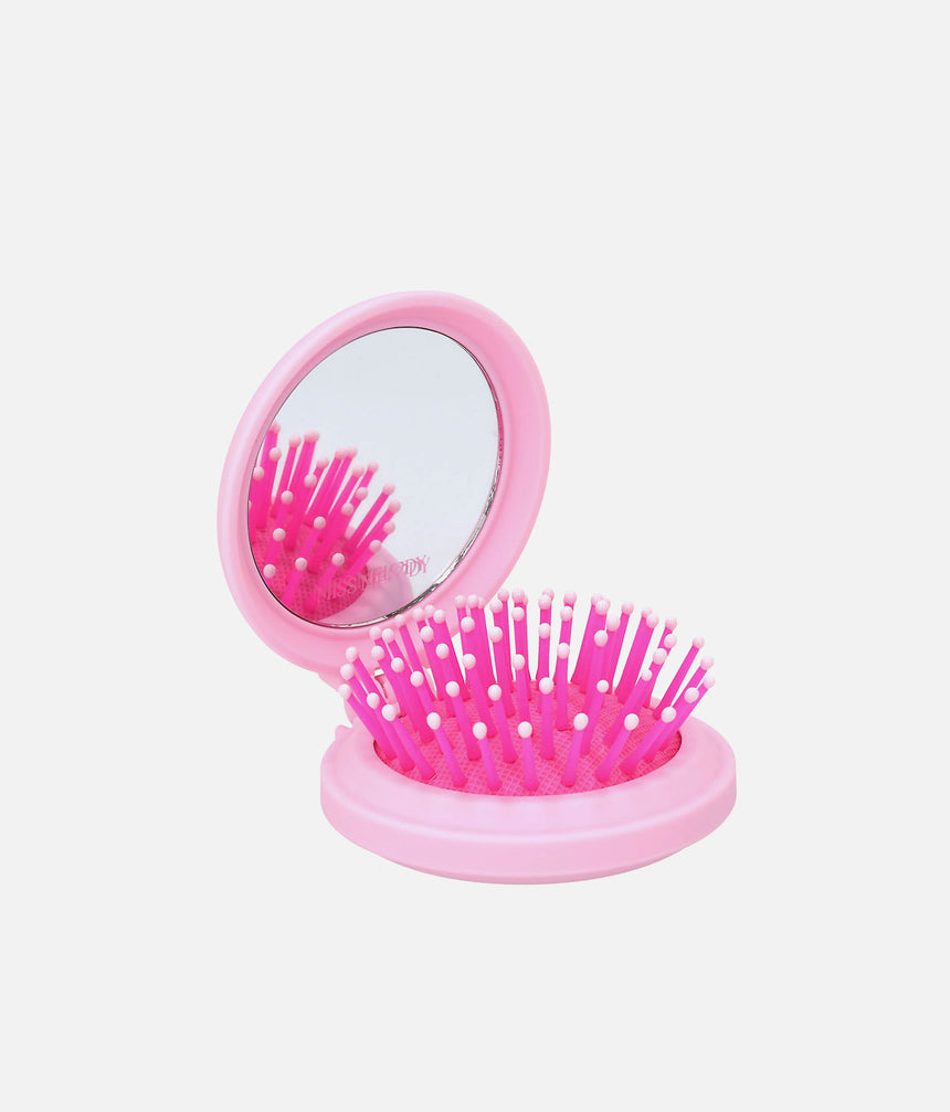 Open pink Miss Melody folding hairbrush showing the built-in mirror and bright pink bristles with pale rounded tips