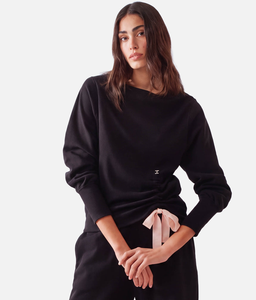 Model wearing Repetto S0797 black side bow sweatshirt with a pale-pink tie, gathered asymmetric hem and black trousers.