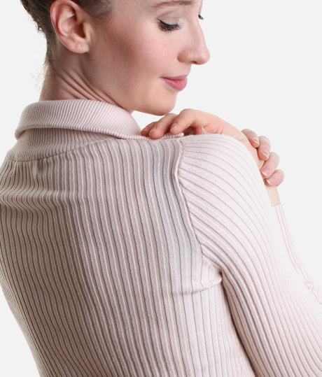 Close-up of a woman wearing a ribbed knit mock neck sweater in a light blush pink color, showing the texture of the fabric and the shoulder seam.