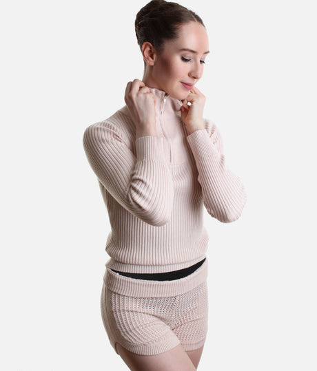 A woman wearing a light pink ribbed knit long-sleeve half-zip top and matching knit shorts, shown against a plain light gray studio background.