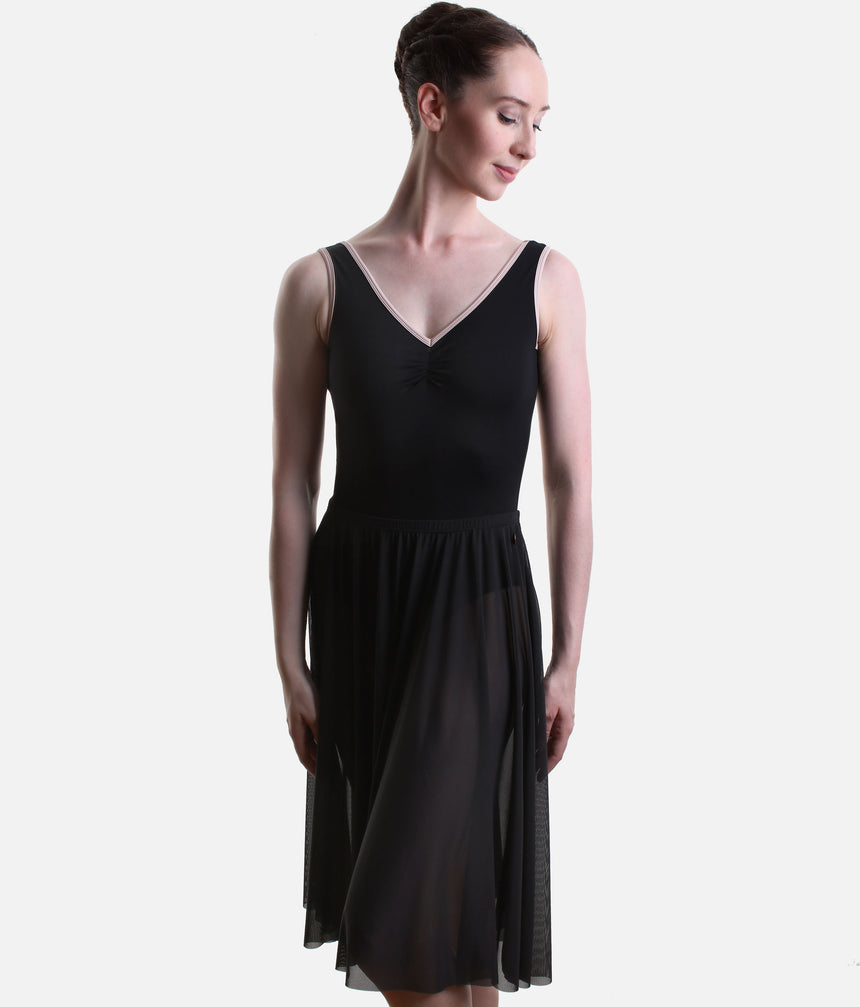 A woman modeling a sleeveless black dance dress with a V-neckline, solid black bodice, and flowing sheer black skirt panels, photographed against a light gray studio background.
