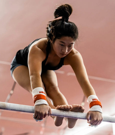 Gymnast using Reisport Elite Protec grips on uneven bars, worn over white wristbands