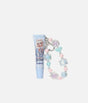 A lip gloss tube in light blue with a character illustration and the text 'Lip gloss' and 'Blueberry', attached to a beaded charm strap with pastel pink, blue, and iridescent beads on a light gray background.