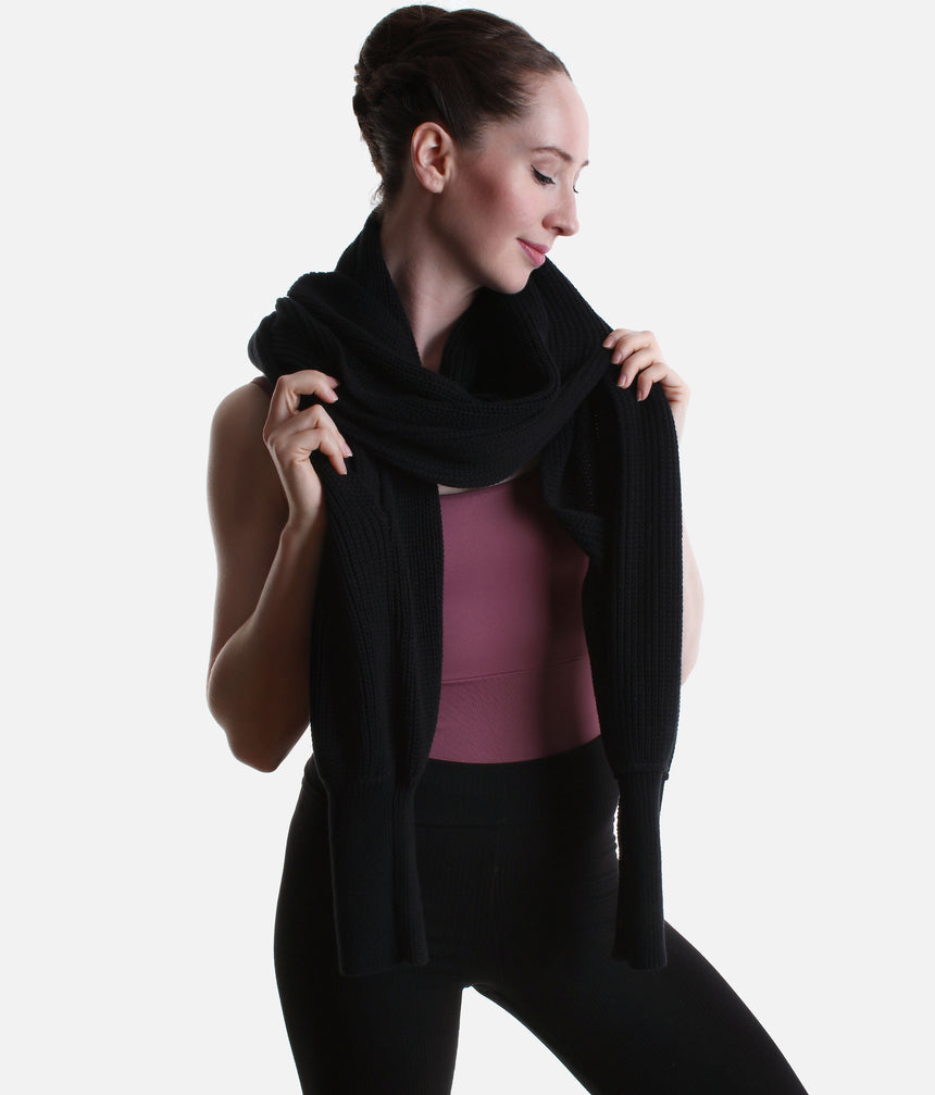 Black Mirella Adagio warm-up scarf worn as a cropped bolero, showing long sleeves and a twisted drape over a plum leotard.