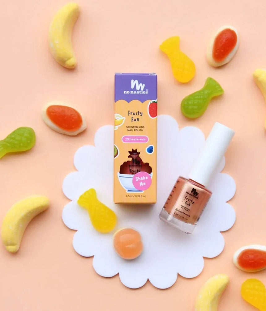 A bottle of 'Fruity Fun' nail polish and its packaging box are displayed on a white scalloped paper plate, surrounded by colorful gummy candies on a pastel peach background.