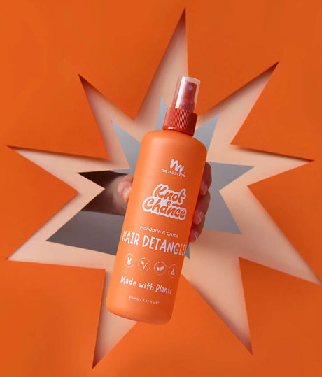 An orange bottle of Knot's Chance Hair Detangler held by a hand, set against a matching orange background with a star-shaped cutout design.