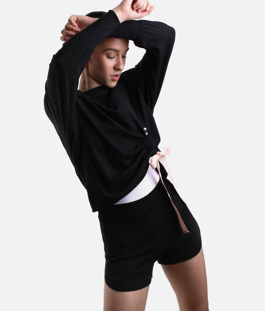 Model wearing Repetto S0797 black side bow sweatshirt with a pale-pink tie, gathered asymmetric hem and black trousers.
