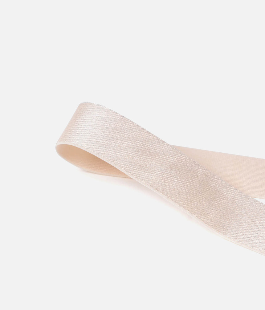 A close-up of a light beige satin ribbon looped in the air against a solid white background.
