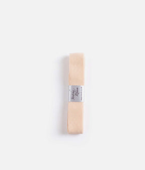 Overhead view of pale peach-pink Tendu Stretchy Ribbon, folded lengthways with its labelled paper band at the centre.