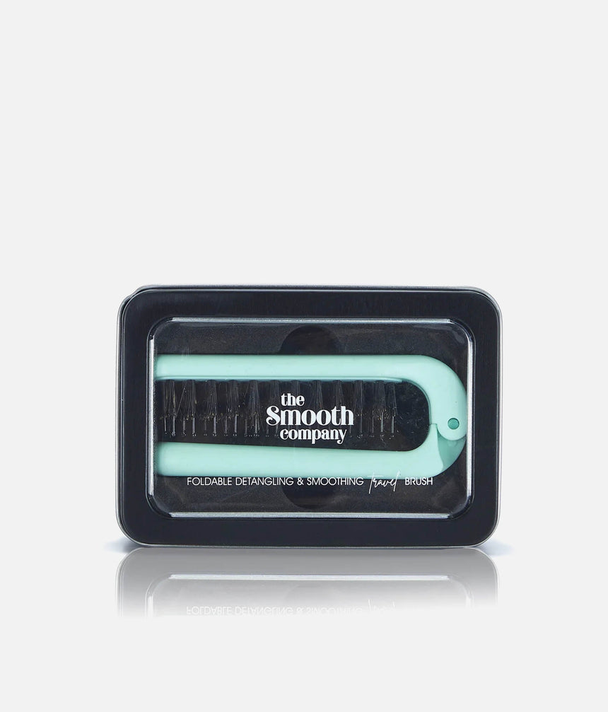 The Smooth Company Foldable Smoothing Travel Brush in mint, shown folded inside its black storage tin.
